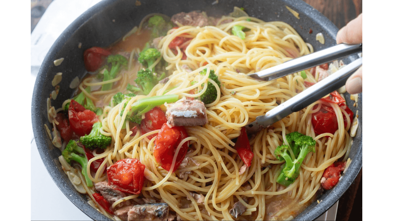 パスタにサバ水煮缶を汁ごと加えて混ぜ合わせる様子