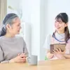 ピンクのエプロンをした介護者が高齢者に質問をしている写真
