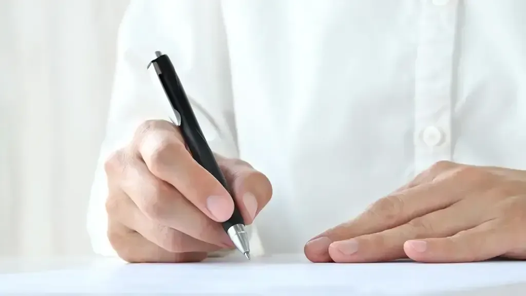 右手にペンを持ち左手で紙をおさえる