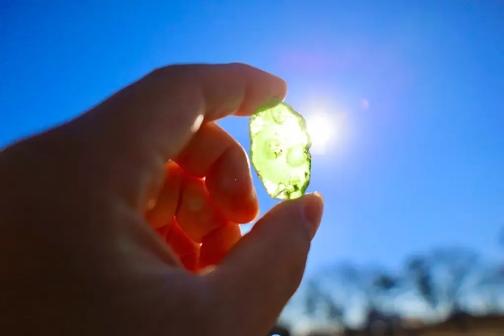 空と太陽の光に緑色の物体をかざした写真
